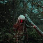 person in brown and black camouflage jacket wearing white helmet standing on brown tree branch during