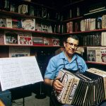 a man sitting in front of a book shelf holding an accordion